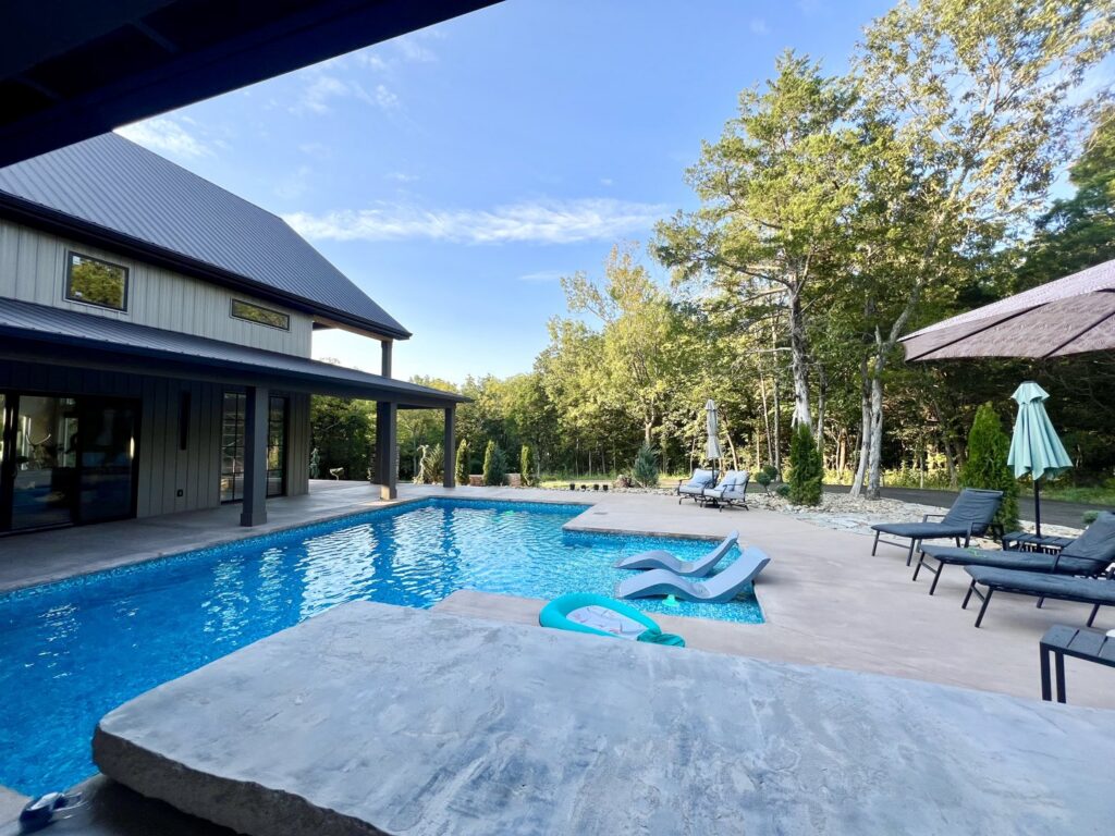 A custom-shaped inground pool with spacious concrete patio and lounge chairs, designed by Riverstone LLC in Bowling Green, KY.