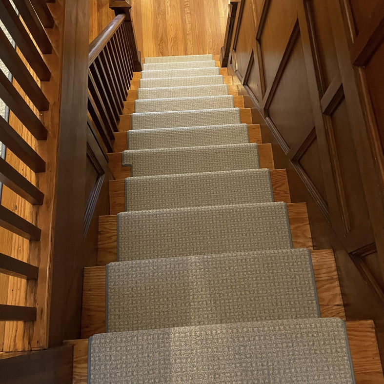Custom carpet runner installed on a wooden staircase, viewed from above, by J MIKE PONTE FLOOR COVERING in Lowell, MA.