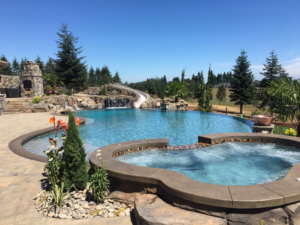 A custom swimming pool with a built-in spa, rock waterfall, and slide by Anderson Poolworks in Wilsonville, OR.
