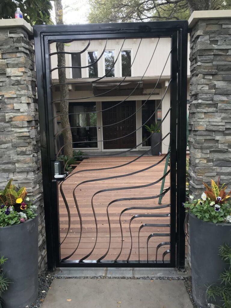 A custom black metal pedestrian gate with a unique wavy design and stone pillars by Craftsman Automatic Gates in Dallas, TX