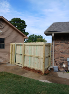 A custom wooden fence enclosure with a gate, built next to a home by Master Fence Builders in Fort Smith, AR.