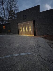 A custom modern wood gate with integrated lighting installed in a brick wall by Precision Fence in Meridian, MS.
