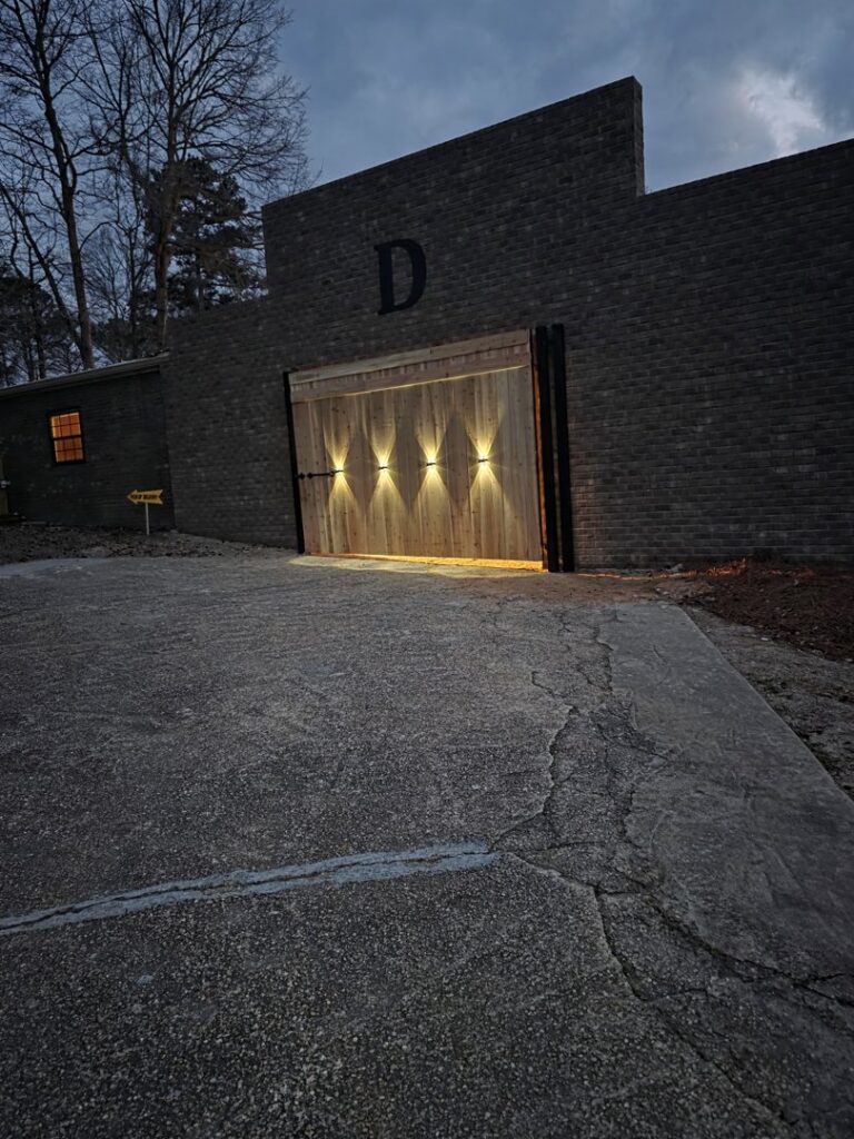 A custom modern wood gate with integrated lighting installed in a brick wall by Precision Fence in Meridian, MS.