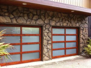 Custom wooden garage doors with frosted glass panels on a stone facade home, installed by Rainier Garage Door in Bellevue, WA.