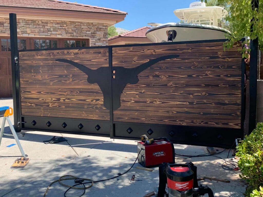 A custom wood and metal driveway gate featuring a longhorn silhouette, installed by Custom Customs Inc. in Henderson, NV.