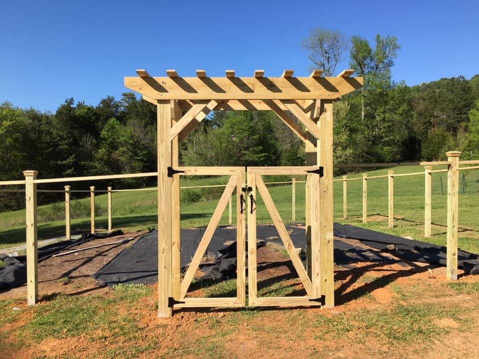 A custom wooden gate with a decorative pergola top, complemented by wire fencing in the background, installed by Holmes Fence Company in Chattanooga, TN.