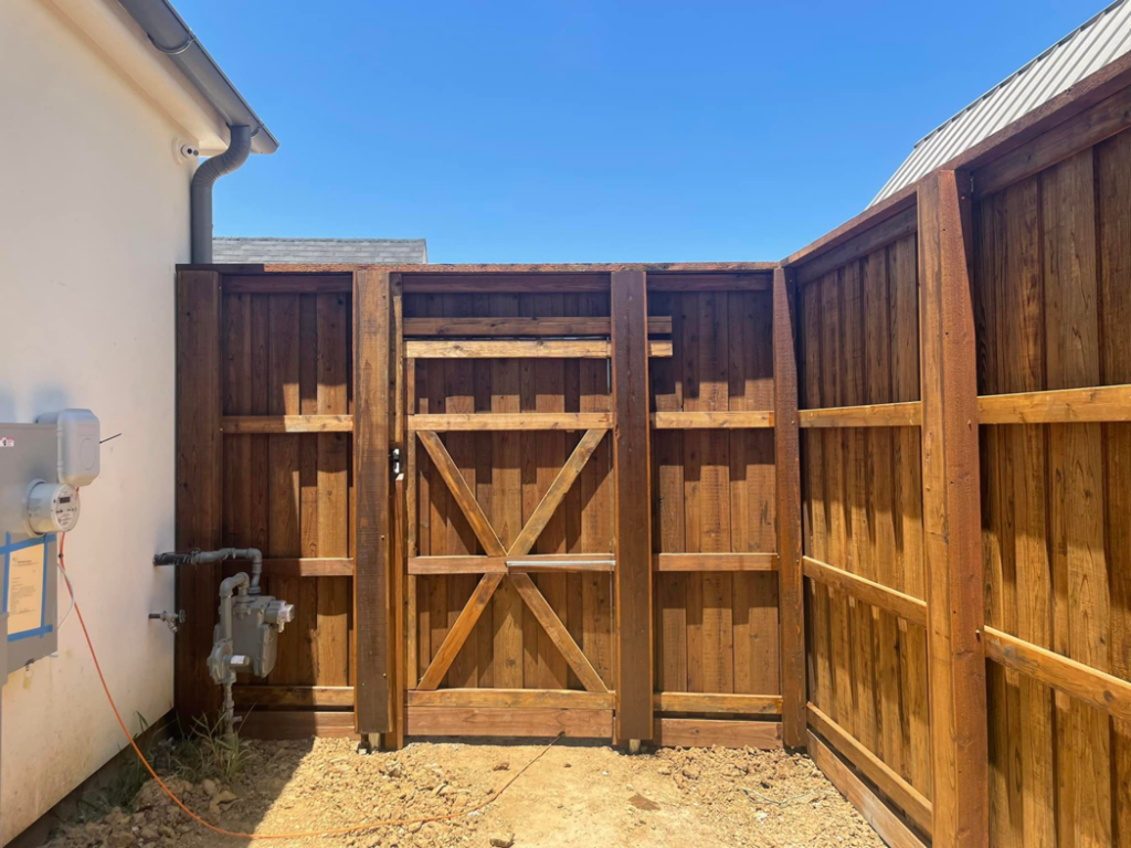 A custom-built wood privacy fence gate installed next to a house by 3M Custom Fence in Lewisville, TX.