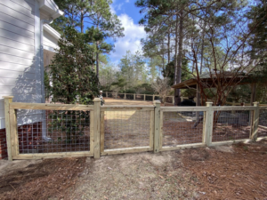 A custom wood and wire mesh fence and gate installed next to a home by Renegade Fencing, LLC in Jacksonville, NC.