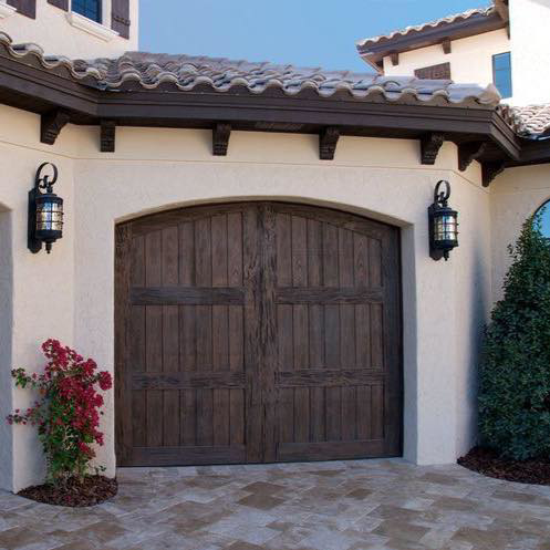 A beautiful custom wooden arched garage door on a stucco home, representing installation services by Heritage Garage Door Service LLC in Phoenix, AZ.