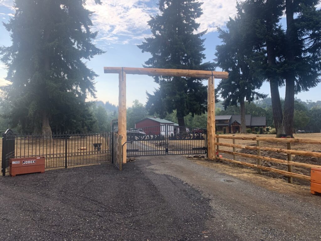 A custom wooden archway gate with decorative black metal gates and a split rail fence installed by PNW FENCE in Lewiston, ID.