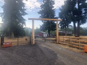 A custom wooden archway gate with decorative black metal gates and a split rail fence installed by PNW FENCE in Lewiston, ID.
