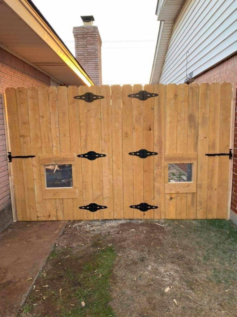 A custom wooden double gate with decorative hinges and small windows installed by TOP TIER FENCE LLC in Oklahoma City, OK.