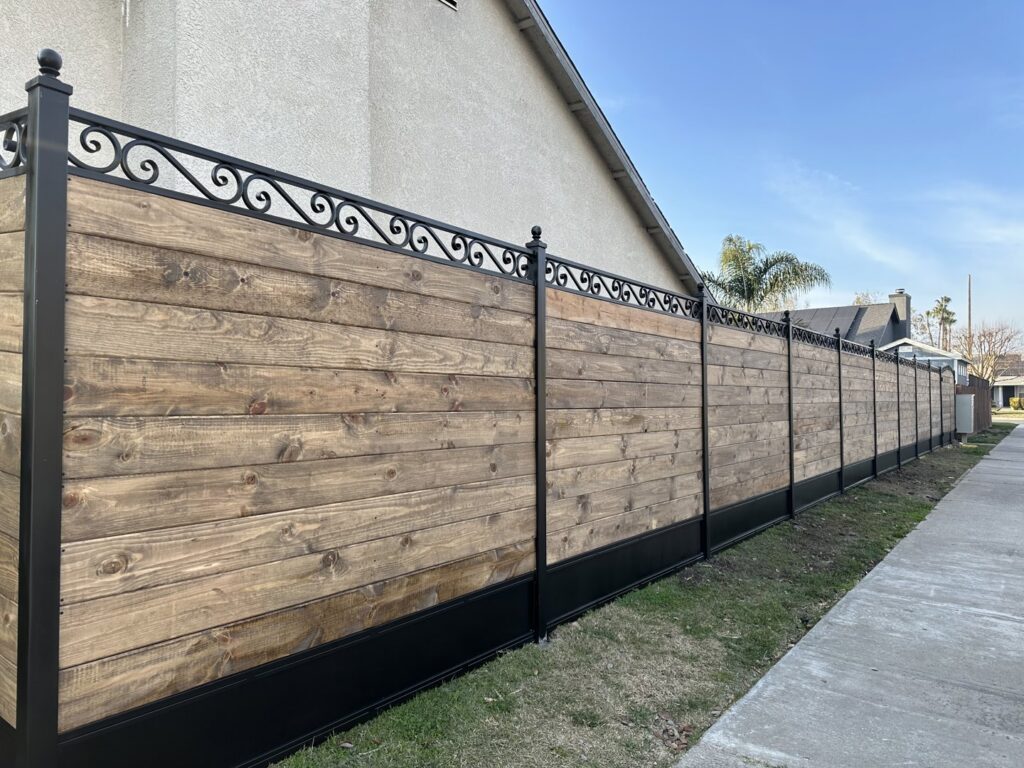 A long custom wooden fence with sturdy iron posts and a decorative top, built by Exclusive Custom Iron Works in Stockton, CA.
