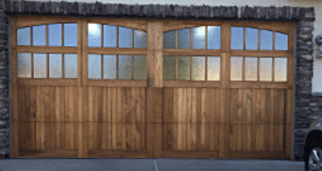 Custom wooden garage doors with arched windows installed on a stone house by Prutch's Garage Door in Page, AZ
