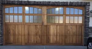 Custom wooden garage doors with arched windows installed on a stone house by Prutch's Garage Door in Page, AZ