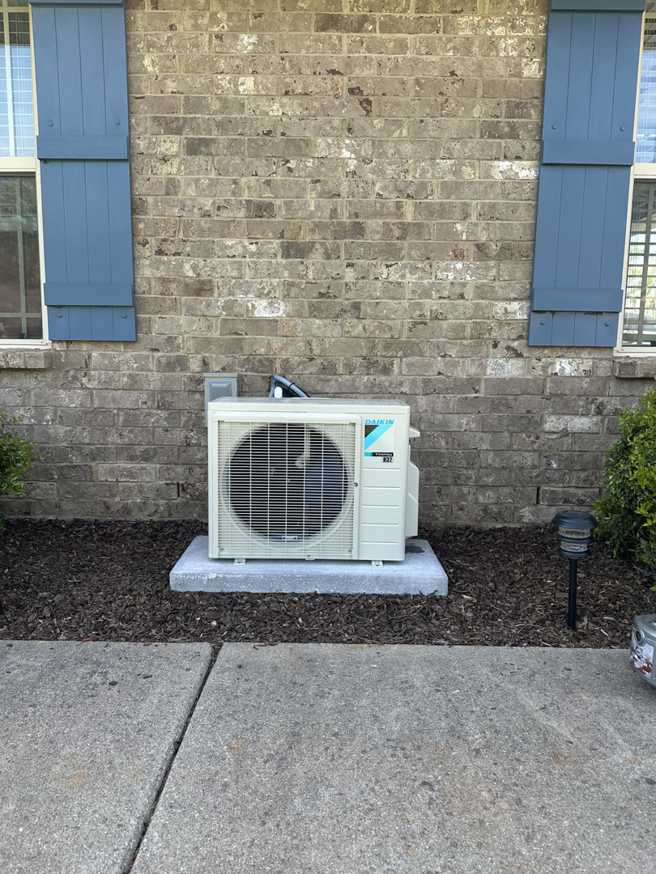 A Daikin mini-split outdoor condenser unit installed next to a brick home by G & N Heating and Cooling in Huntsville, AL.