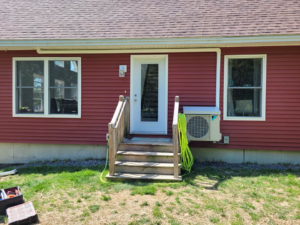 A Daikin mini-split outdoor unit installed on the side of a red house by Maine Thermal Energy Services in Ellsworth, ME