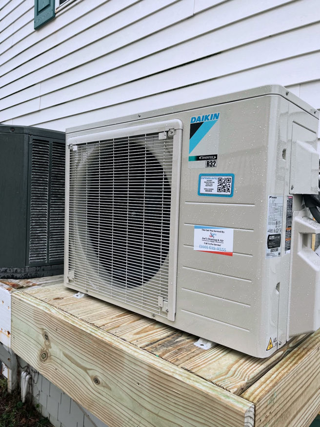 A Daikin outdoor HVAC condenser unit installed on a wooden deck by Joe's Heating & Air Repair LLC in Surf City, NC