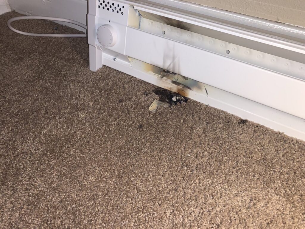 A damaged baseboard heater with burn marks on the carpet, indicating a heating repair job by R. Davis Mechanical in Pittsburgh, PA