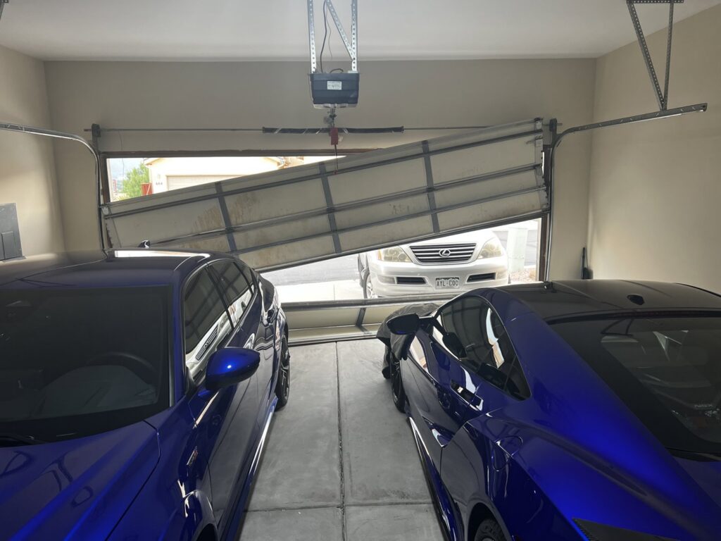 A severely damaged and bent garage door inside a residential garage, indicating a need for repair or replacement by Million Garage Door Services in Colorado Springs, CO.
