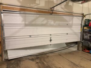 A garage door with a bent and damaged bottom panel, indicating a need for repair from Greeley garage door repair in Greeley, CO.
