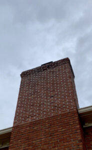A damaged brick chimney showing wear at the top, indicating need for repair by Professional Fireplaces and Chimney Sweeps in Huntsville, AL.
