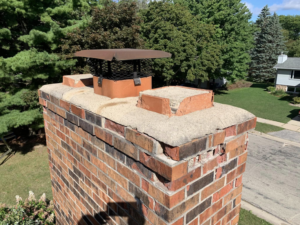 A damaged brick chimney top with a cap, inspected by The Chimney Sweep in Stafford, VA.