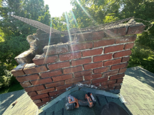 A severely damaged brick chimney on a roof requiring repair, serviced by The Chimney Guys in Jackson, TN.