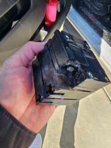 A hand holding a severely damaged and burnt circuit breaker, indicating a repair job by Elite Electric Company in Melrose Park, IL