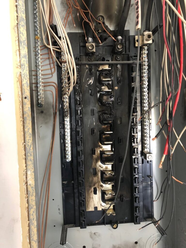 A severely damaged and burnt electrical panel interior, indicating a need for repair by McCall Enterprises in Atlanta, GA.