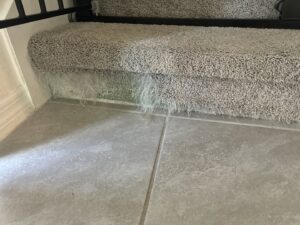 Underside of a carpeted stair showing loose fibers and water damage, requiring repair from Mr. Carpet Cleaning Orlando, FL.