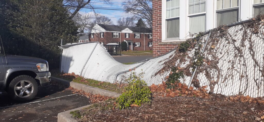 A damaged chain link fence covered in vines, indicating a potential repair or replacement job by Brothers Fence in Elizabeth, NJ.