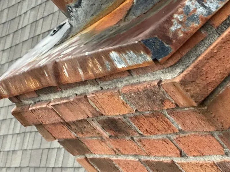 A close-up view of a damaged and rusty chimney crown and flashing, highlighting repair services from The Chimney Doctor in Louisville, KY.