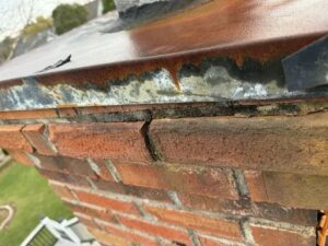 A close-up of a damaged chimney crown and flashing with a visible crack, showing repair needs by The Chimney Doctor in Louisville, KY.