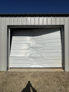 A severely damaged white commercial garage door needing repair by Entry Garage Door in Shawnee, OK.