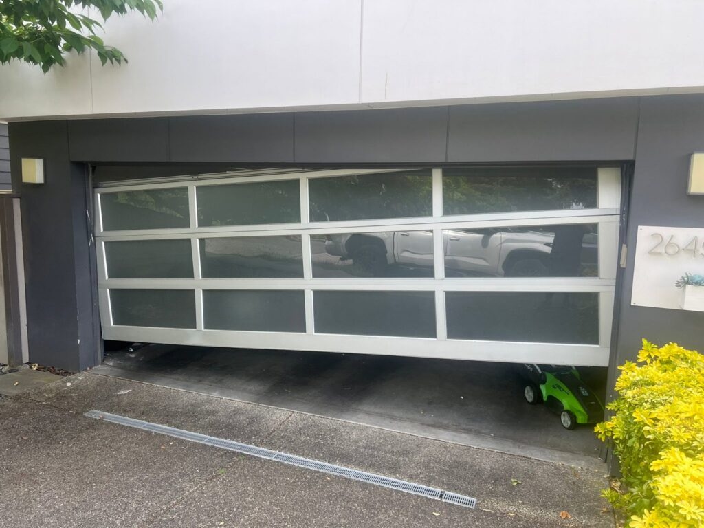 A damaged or off-track garage door, partially open and crooked, requiring repair from 101 Garage Doors in Phoenix, AZ.