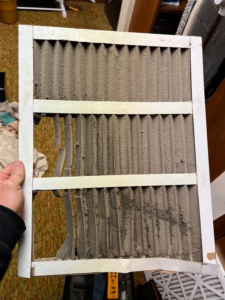 A hand holding a damaged and dirty HVAC air filter, highlighting the need for professional service from Elite Air Pros in Yukon, OK.