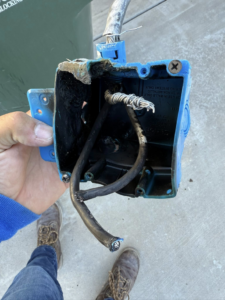 A hand holding a damaged electrical box with burnt wires, indicating a repair by Dependable Sparky Electric in Peoria, AZ