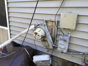 A severely damaged electrical meter and service entrance on the side of a house, requiring urgent repair from AA Electric Contractors in Chicago, IL.