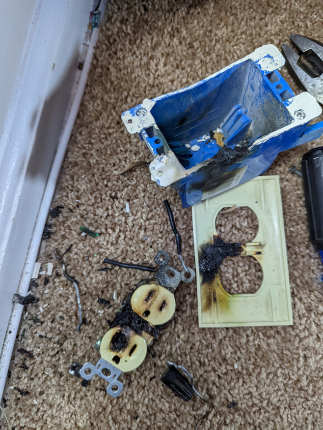 A damaged electrical outlet and junction box on a carpeted floor, indicating a repair job by The Wire Guy in San Jose, CA.