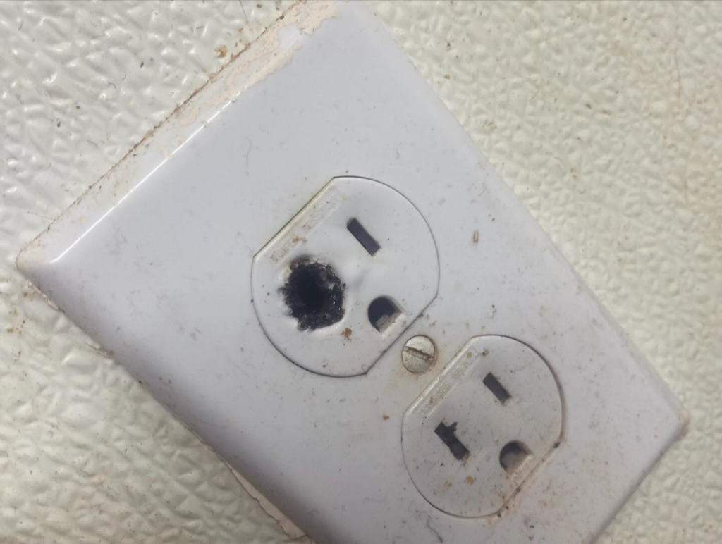 A close-up of a damaged electrical outlet with a burn mark, indicating a need for repair by Island Power Company LLC in South Kingstown, RI.