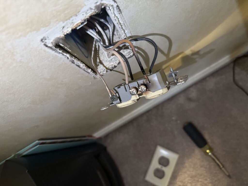 A damaged electrical outlet with exposed wiring, indicating a repair job by Conductive Electrical Contracting in Smyrna, DE.