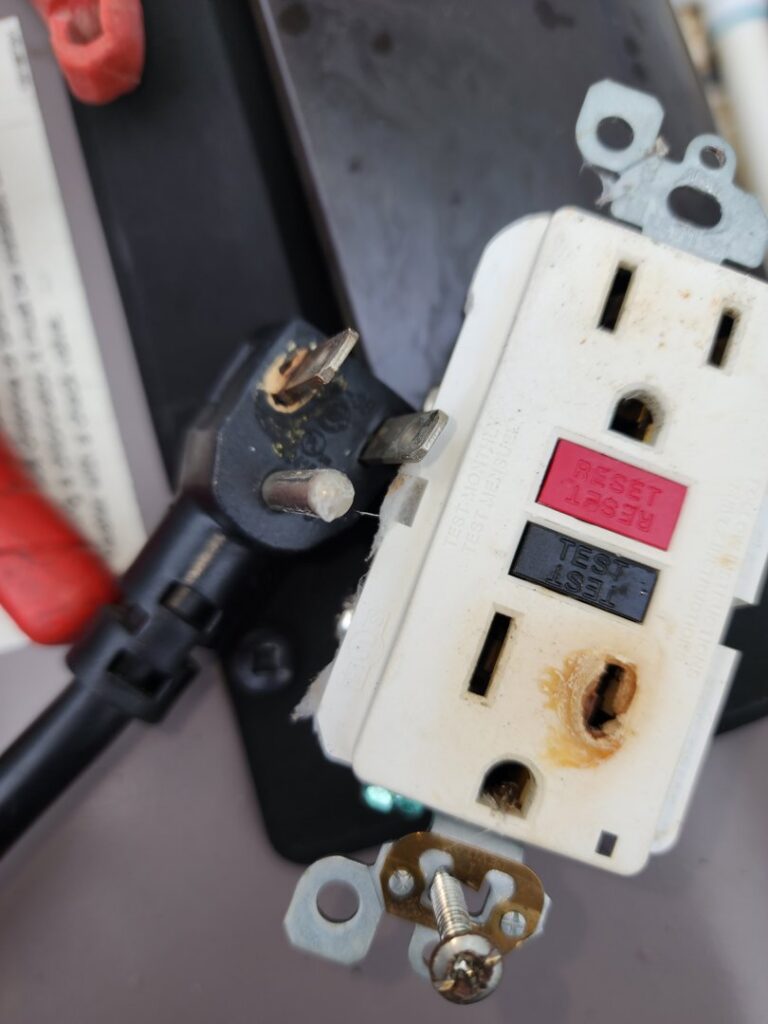 A damaged and burnt electrical GFCI outlet and plug, indicating a hazardous electrical repair needed from York Electrical Services in York, PA.