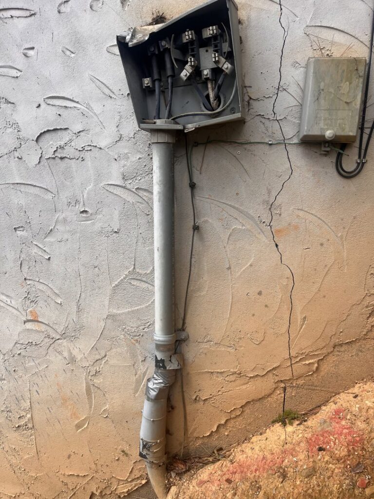 A damaged exterior electrical box and conduit on a stucco wall, requiring repair by Shocking Solutions in Knoxville, TN.