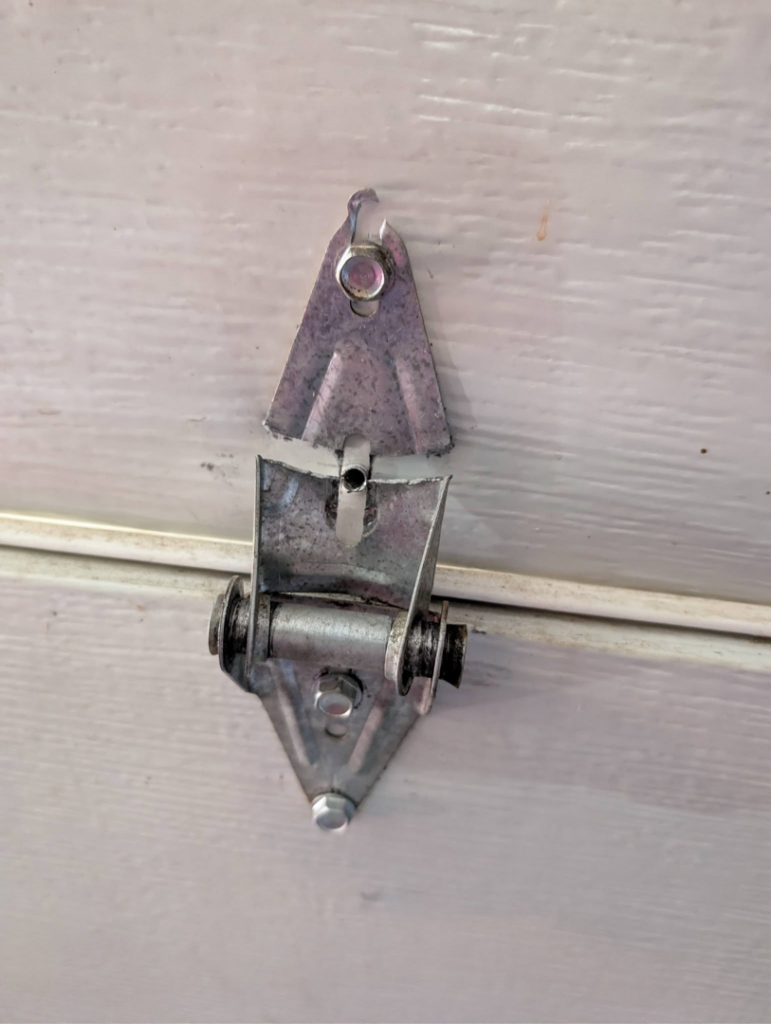 A close-up view of a damaged garage door hinge, requiring repair by Garage Doors & Remodeling LLC in Blue Springs, MO