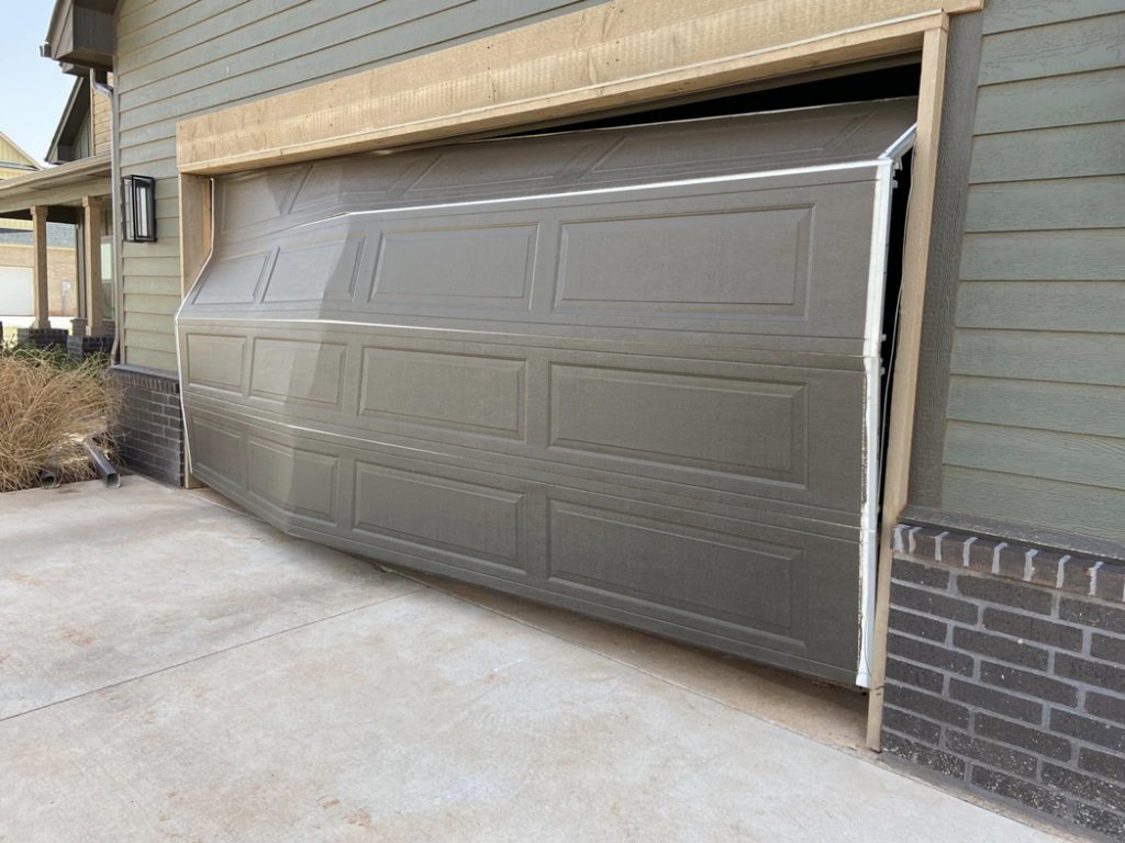 A damaged garage door that is off its tracks on one side, requiring repair from Unhinged Garage Doors LLC in Oklahoma City, OK.
