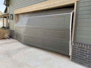 A damaged garage door that is off its tracks on one side, requiring repair from Unhinged Garage Doors LLC in Oklahoma City, OK.