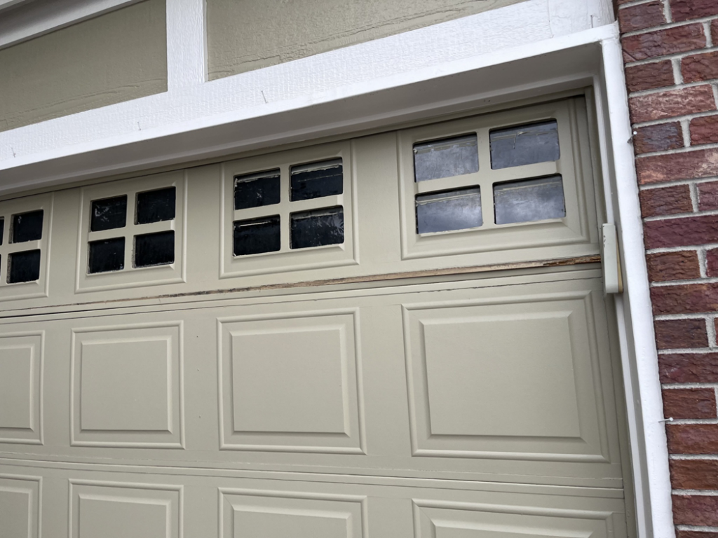 Close-up of a damaged garage door panel with windows, showing a need for repair from Pham Garage Door Service & Repair in Arvada, CO.