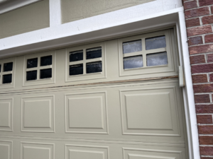 Close-up of a damaged garage door panel with windows, showing a need for repair from Pham Garage Door Service & Repair in Arvada, CO.