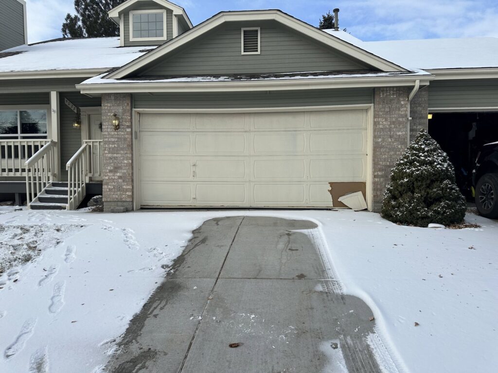 A damaged garage door in the snow, indicating a need for repair or replacement by Strongdoor garage in Denver, CO.